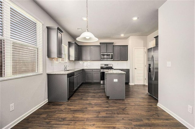 kitchen with a kitchen island, dark hardwood / wood-style flooring, hanging light fixtures, light stone counters, and stainless steel appliances