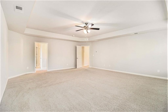 spare room with a raised ceiling, light carpet, and ceiling fan