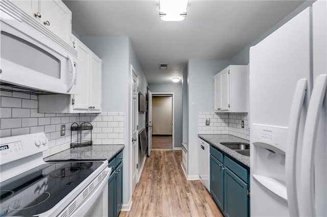 kitchen with light wood-style flooring, blue cabinets, white appliances, white cabinetry, and dark stone countertops