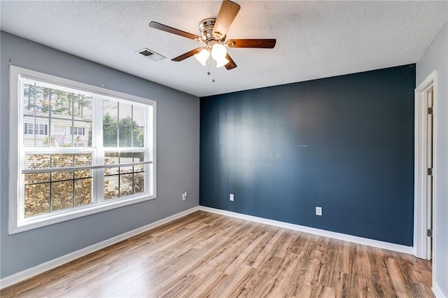 spare room featuring light wood-type flooring, a ceiling fan, baseboards, and a textured ceiling