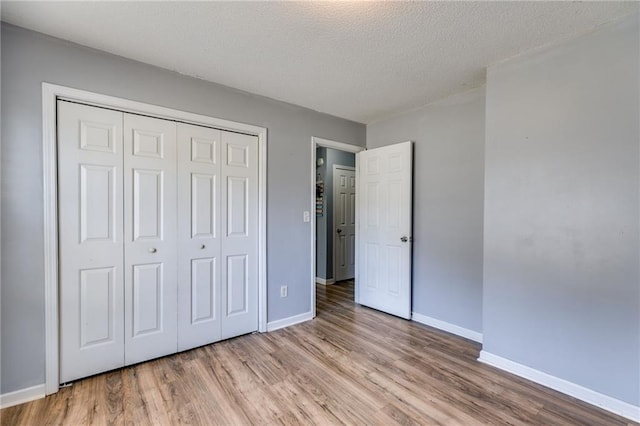 unfurnished bedroom with a textured ceiling, a closet, light wood-style flooring, and baseboards