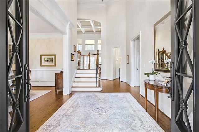 entrance foyer with arched walkways, coffered ceiling, stairway, dark wood-style floors, and beamed ceiling