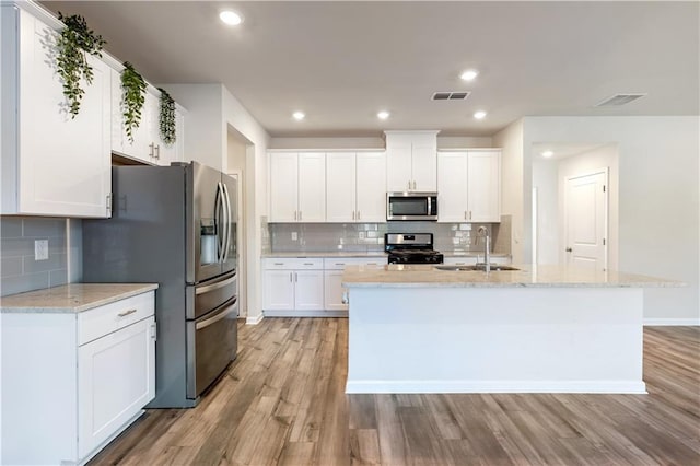 kitchen featuring white cabinetry, stainless steel appliances, a kitchen island with sink, and light stone counters