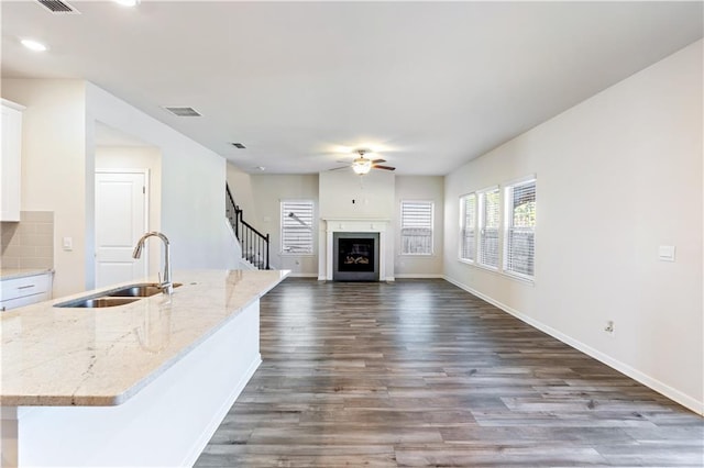 kitchen with sink, white cabinets, a kitchen island with sink, light stone counters, and dark wood-type flooring