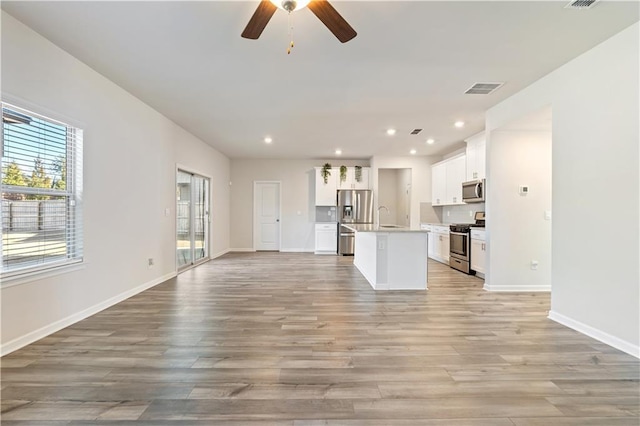 kitchen featuring ceiling fan, stainless steel appliances, white cabinets, a center island with sink, and light wood-type flooring