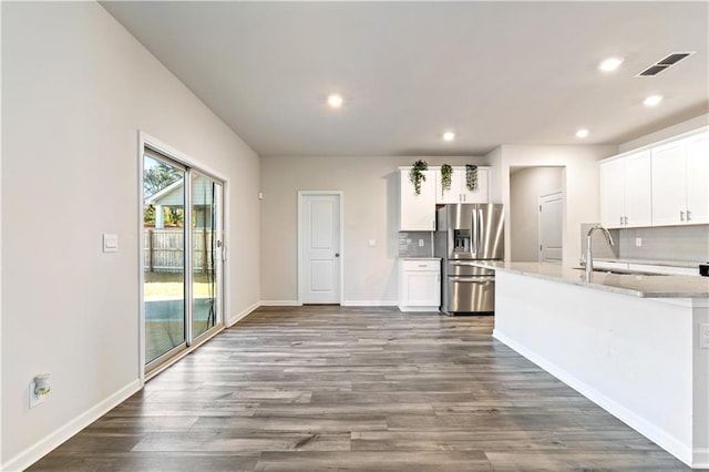 kitchen featuring sink, white cabinets, backsplash, stainless steel refrigerator with ice dispenser, and light stone countertops