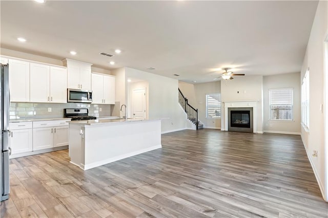 kitchen with appliances with stainless steel finishes, tasteful backsplash, an island with sink, white cabinets, and light wood-type flooring