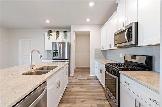 kitchen featuring appliances with stainless steel finishes, white cabinetry, sink, backsplash, and light stone counters