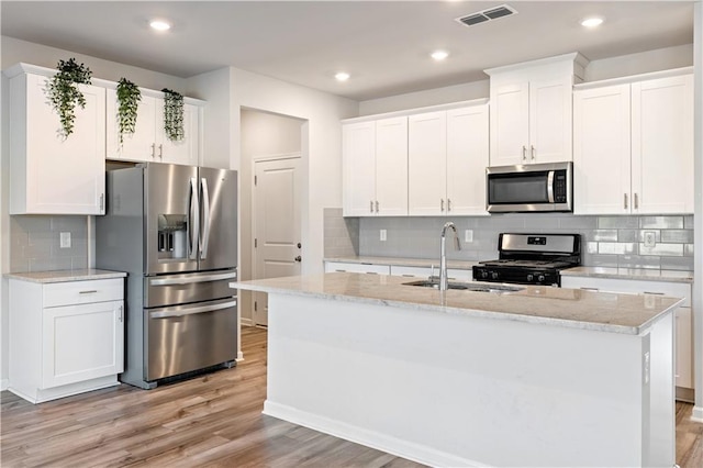 kitchen featuring sink, stainless steel appliances, light stone counters, white cabinets, and a center island with sink