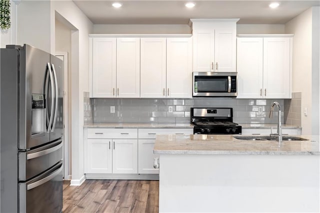 kitchen with sink, light hardwood / wood-style flooring, stainless steel appliances, light stone countertops, and white cabinets