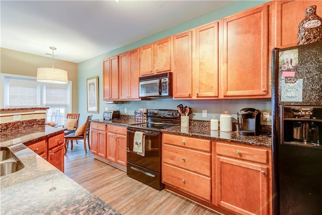 kitchen featuring a sink, light wood-style floors, dark stone counters, black appliances, and hanging light fixtures