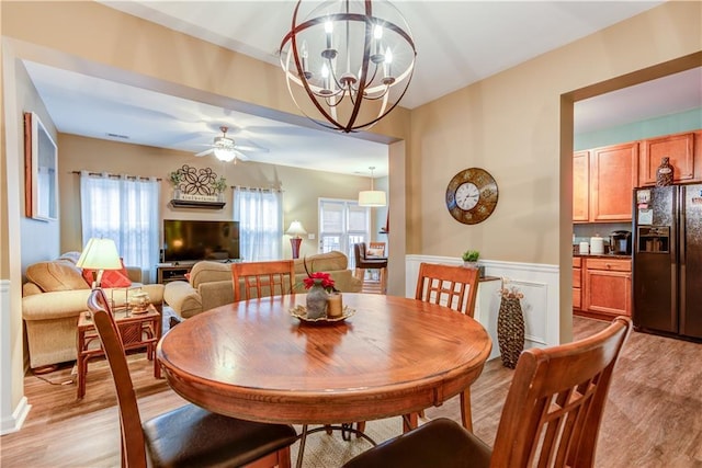 dining room with a wainscoted wall, ceiling fan with notable chandelier, and light wood-type flooring