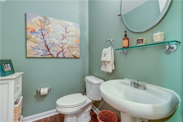half bathroom featuring baseboards, wood finished floors, a sink, and toilet