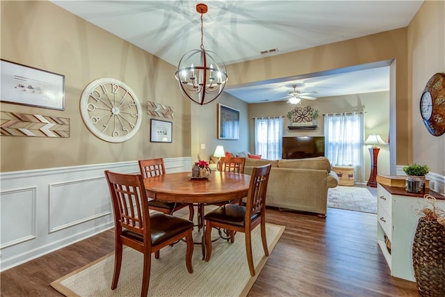 dining space featuring visible vents, a wainscoted wall, dark wood-style floors, and ceiling fan with notable chandelier