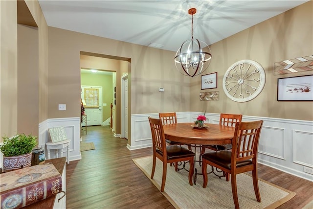dining room featuring wainscoting, a decorative wall, a notable chandelier, and dark wood-type flooring