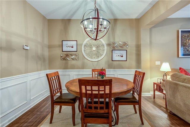 dining space featuring a wainscoted wall, wood finished floors, a chandelier, and a decorative wall
