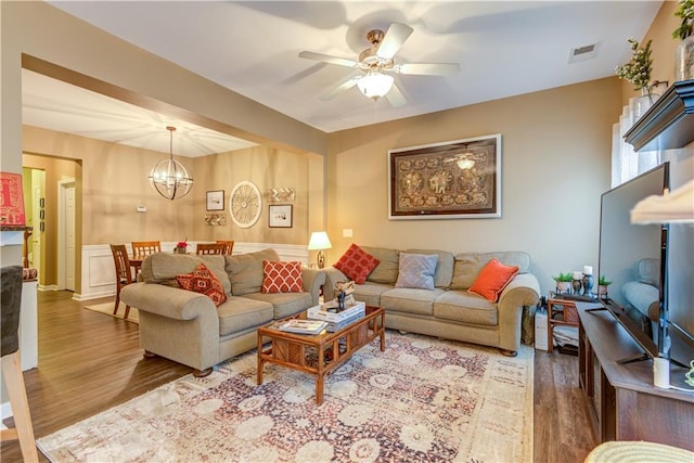 living area featuring wood finished floors, visible vents, and ceiling fan with notable chandelier