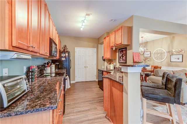 kitchen featuring kitchen peninsula, black appliances, dark stone countertops, light wood-type flooring, and a kitchen bar