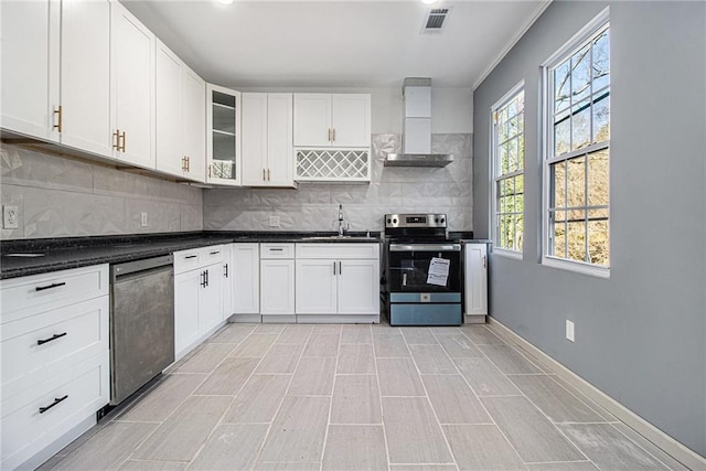 kitchen featuring sink, stainless steel electric range oven, wall chimney range hood, decorative backsplash, and white cabinets