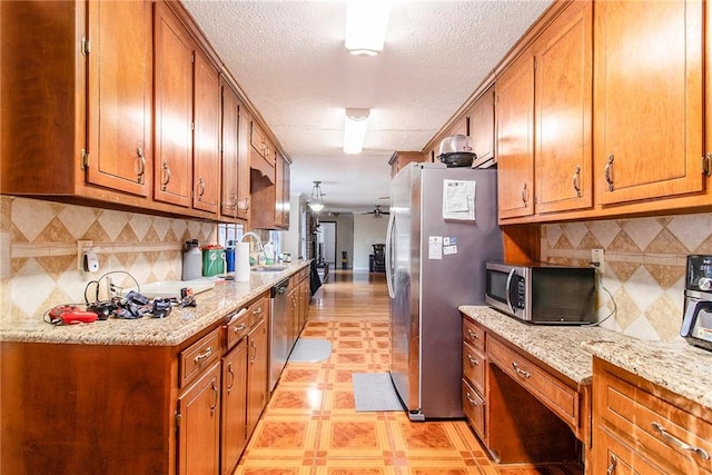 kitchen with a ceiling fan, brown cabinets, light stone countertops, stainless steel appliances, and light floors
