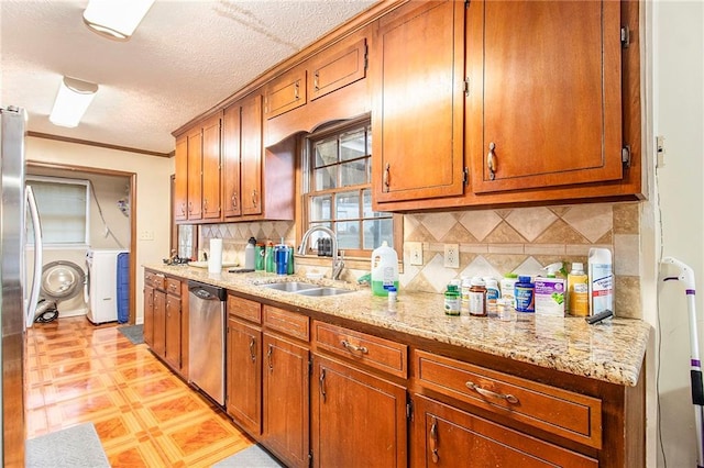 kitchen with light stone counters, brown cabinets, appliances with stainless steel finishes, a sink, and independent washer and dryer