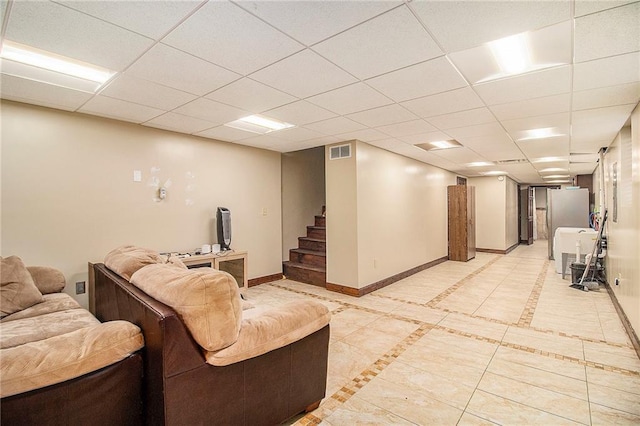 finished below grade area featuring stairway, visible vents, baseboards, and a drop ceiling