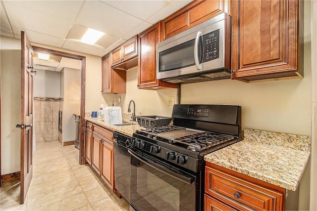 kitchen with a wainscoted wall, light stone countertops, a paneled ceiling, black appliances, and a sink