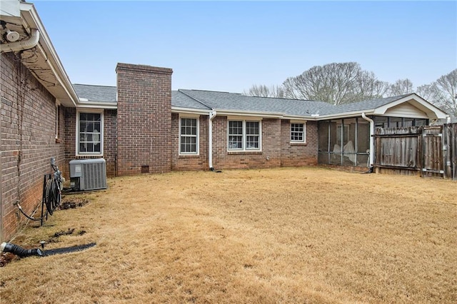 back of property featuring brick siding, a chimney, central air condition unit, a lawn, and a sunroom