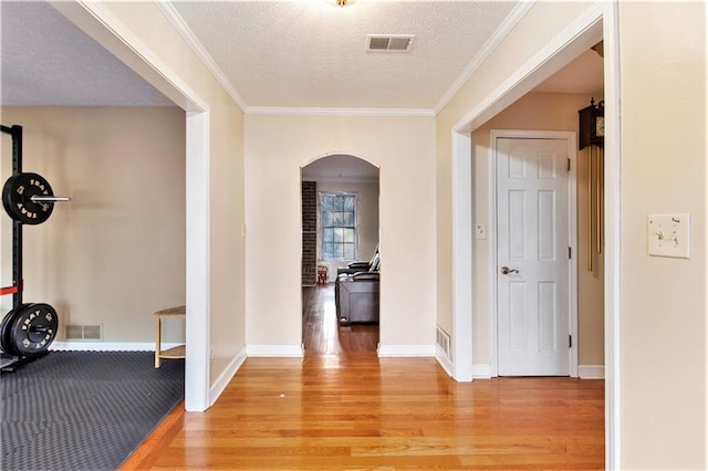 interior space featuring arched walkways, visible vents, light wood-style flooring, and a textured ceiling