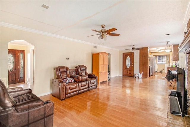 living area featuring arched walkways, ceiling fan, light wood-style flooring, baseboards, and ornamental molding