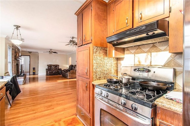 kitchen featuring under cabinet range hood, open floor plan, light wood finished floors, brown cabinetry, and gas range