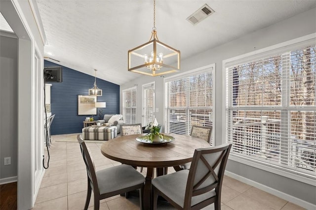 dining room with light tile patterned floors, baseboards, visible vents, lofted ceiling, and an accent wall