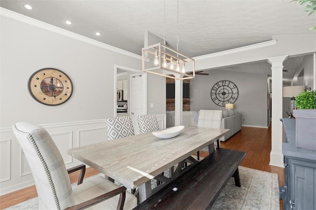 dining space with a wainscoted wall, a decorative wall, an inviting chandelier, ornamental molding, and wood finished floors