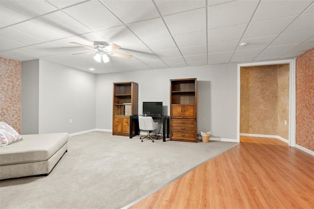 carpeted home office with ceiling fan, baseboards, a drop ceiling, and wood finished floors