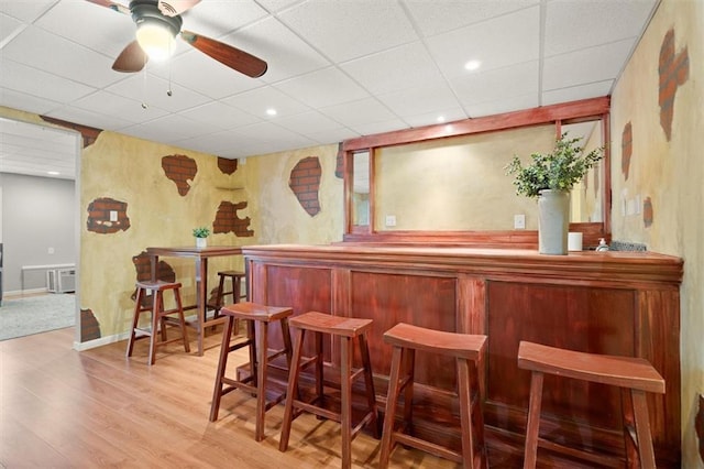 bar with a ceiling fan, a paneled ceiling, light wood-style flooring, a bar, and recessed lighting