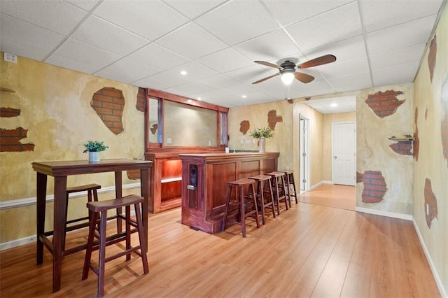 bar featuring a bar, light wood-type flooring, and a paneled ceiling