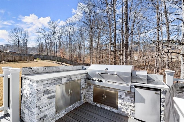 wooden terrace with exterior kitchen, fence, and area for grilling