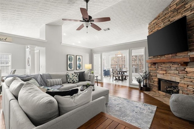 living room with a fireplace, visible vents, a ceiling fan, a textured ceiling, and wood finished floors