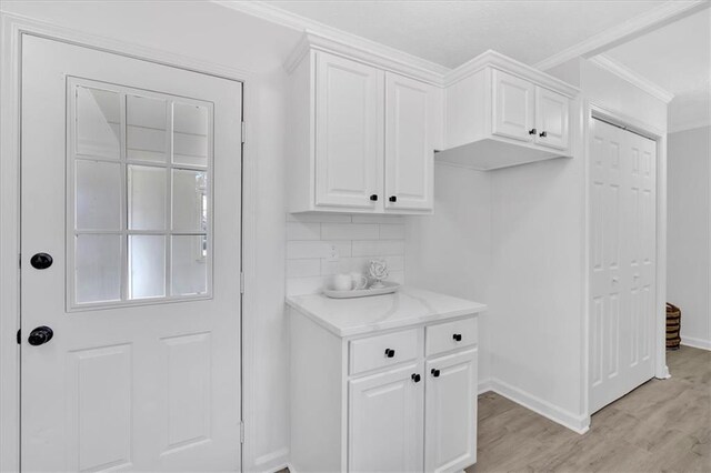 interior space with tasteful backsplash, light stone countertops, ornamental molding, light wood-style flooring, and white cabinets