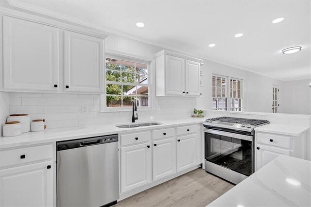 kitchen with a sink, tasteful backsplash, white cabinetry, light wood-style floors, and appliances with stainless steel finishes