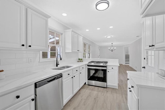 kitchen featuring light wood finished floors, a peninsula, a sink, stainless steel appliances, and white cabinets