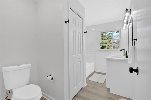 bathroom featuring baseboards, toilet, wood finished floors, and vanity