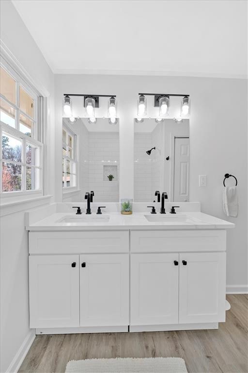 full bathroom featuring double vanity, wood finished floors, tiled shower, and a sink