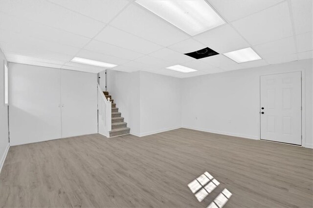 finished basement featuring a drop ceiling, wood finished floors, and stairs