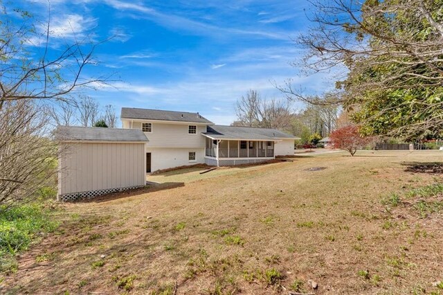 back of property featuring a yard, a sunroom, an outbuilding, and a shed
