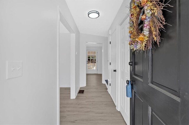 hallway with visible vents, baseboards, and light wood-style flooring
