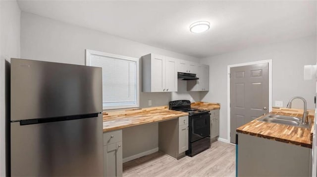 kitchen featuring black range with electric stovetop, under cabinet range hood, freestanding refrigerator, wood counters, and a sink