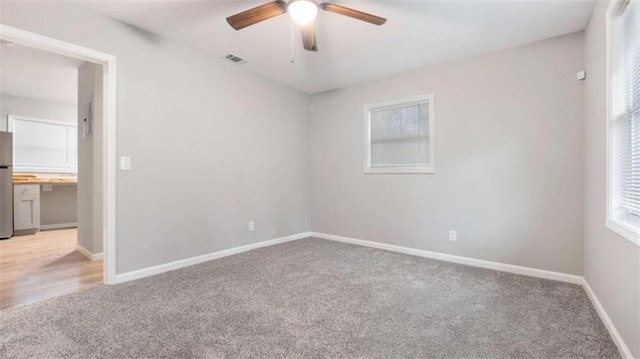 unfurnished room featuring light carpet, visible vents, baseboards, and ceiling fan