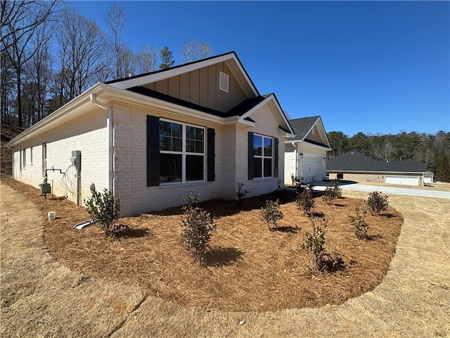 view of side of property featuring driveway, a garage, board and batten siding, and brick siding