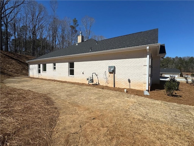 back of property with brick siding, a chimney, and a shingled roof